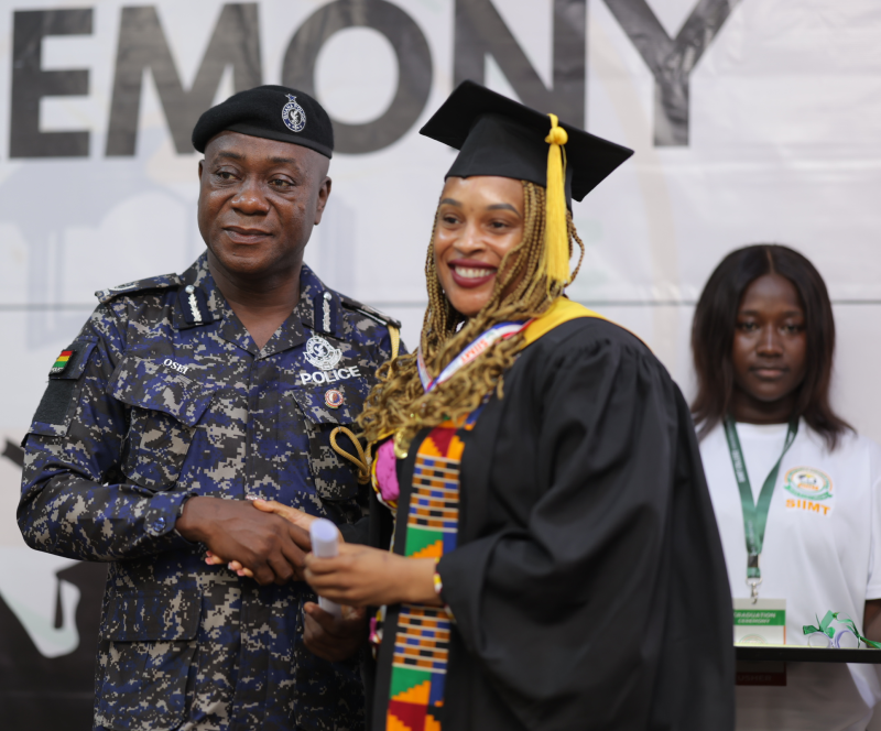 A graduate in a black gown and kente stole shaking hands with a uniformed officer at the SIIMT Graduation 2025