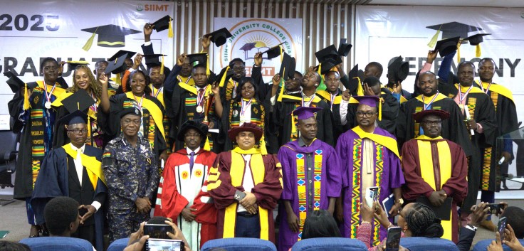 Graduates and officials in academic gowns posing on stage, some raising their hands, at the SIIMT Graduation 2025