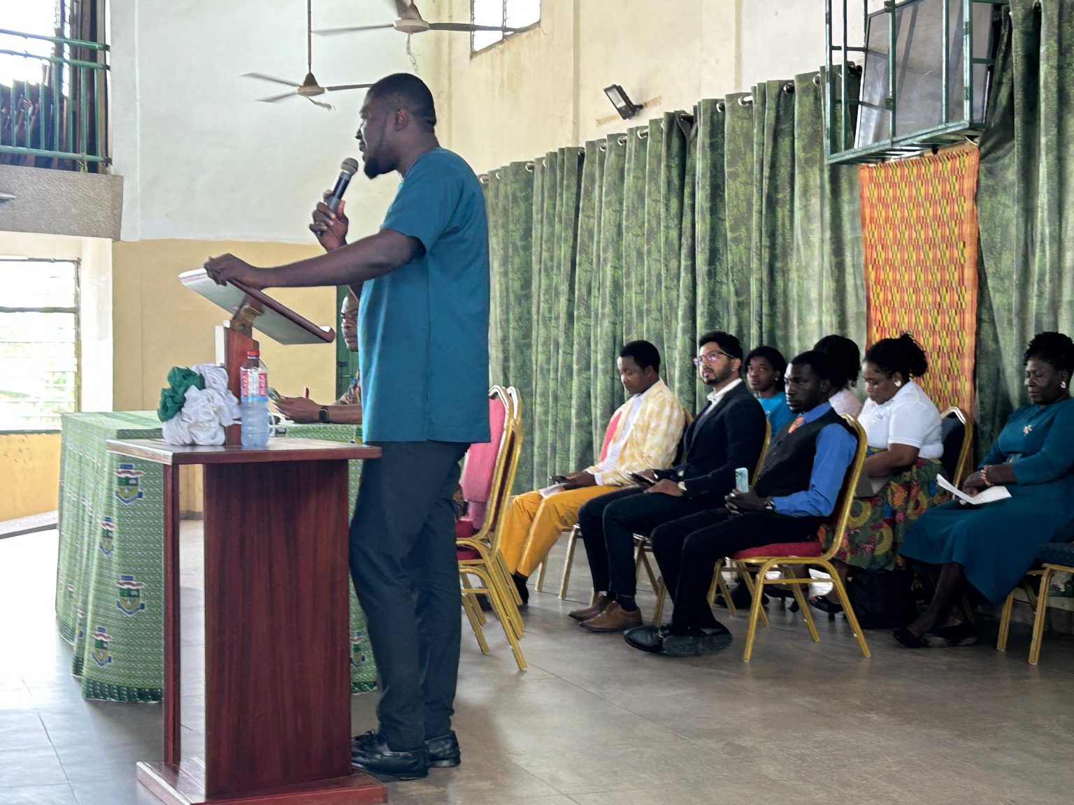A speaker addressing the hall while staff sit beside him at the SIIMT orientation at Nungua SHS
