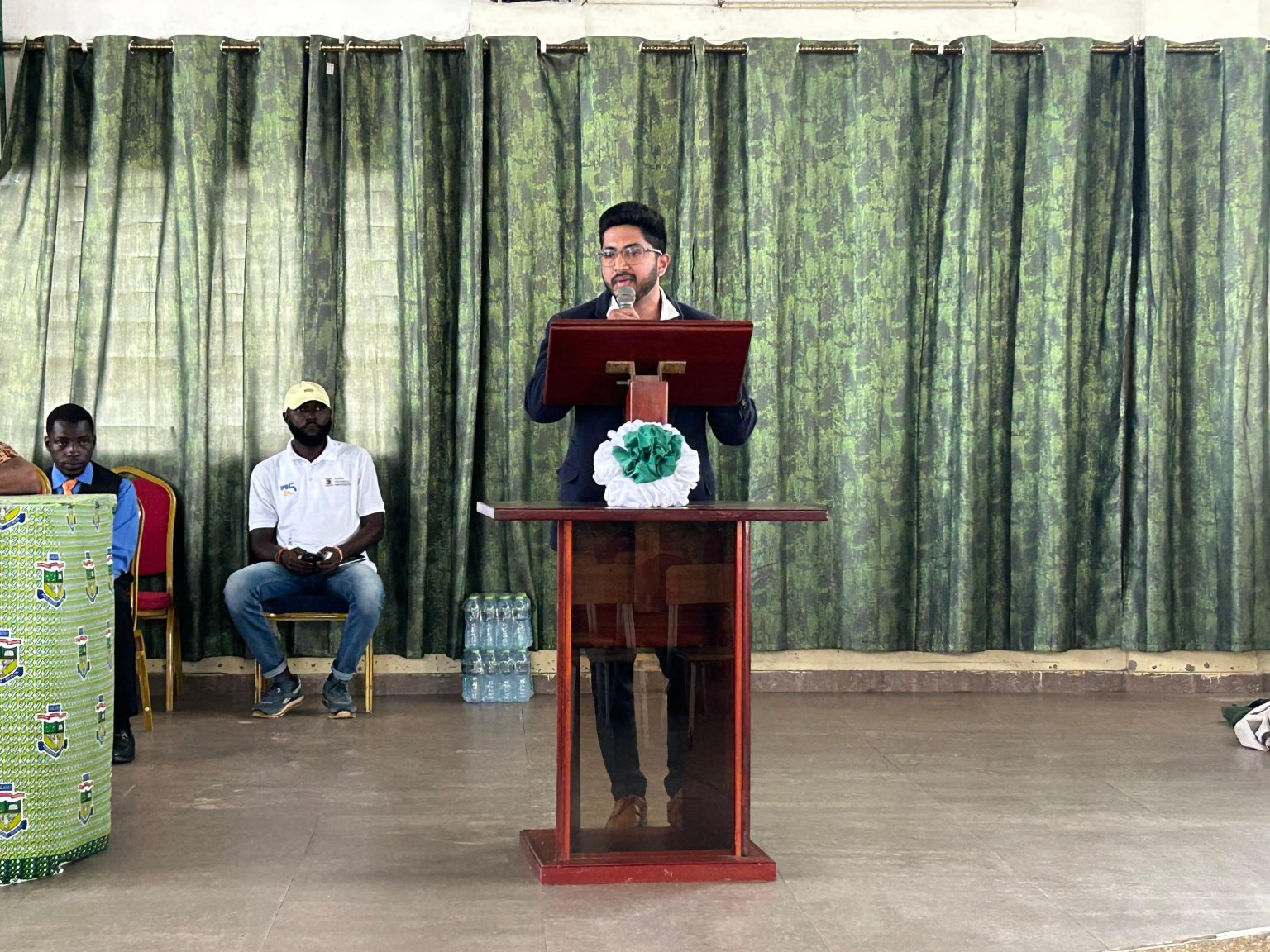 A speaker at a lectern in front of a green curtain at the orientation at Nungua SHS